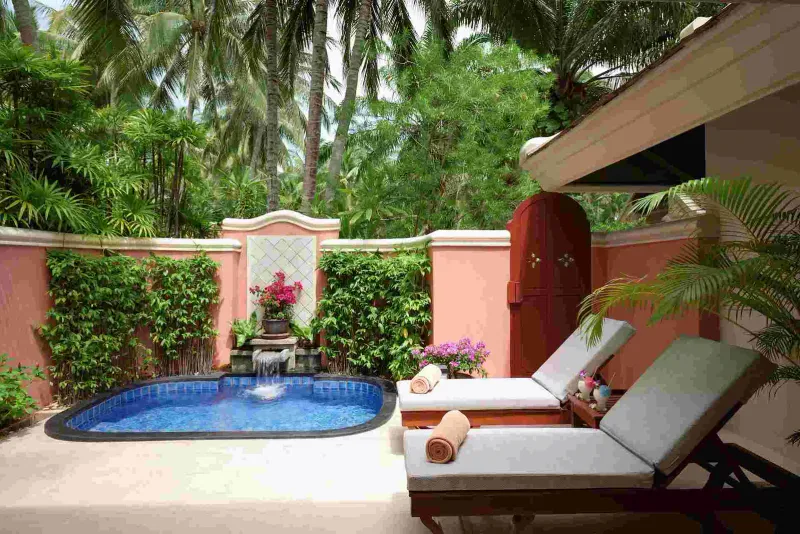 Petite piscine d'une villa de jardin close de murs avec cascade, transats et palmiers à Santiburi Koh Samui