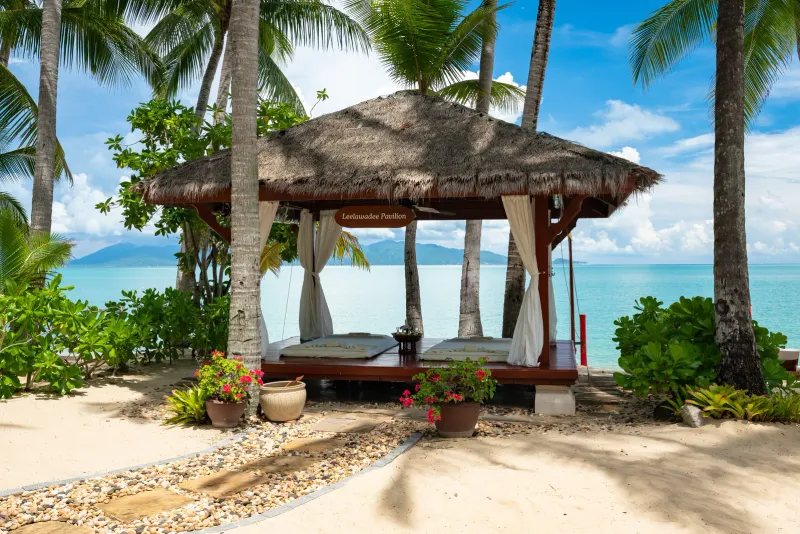 Pavillon de massage au toit de chaume et rideaux blancs face à la baie turquoise à Santiburi Koh Samui