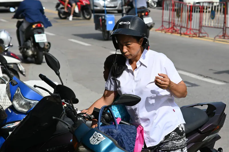 Donna con casco jet nero accanto a scooter parcheggiati in una strada thailandese