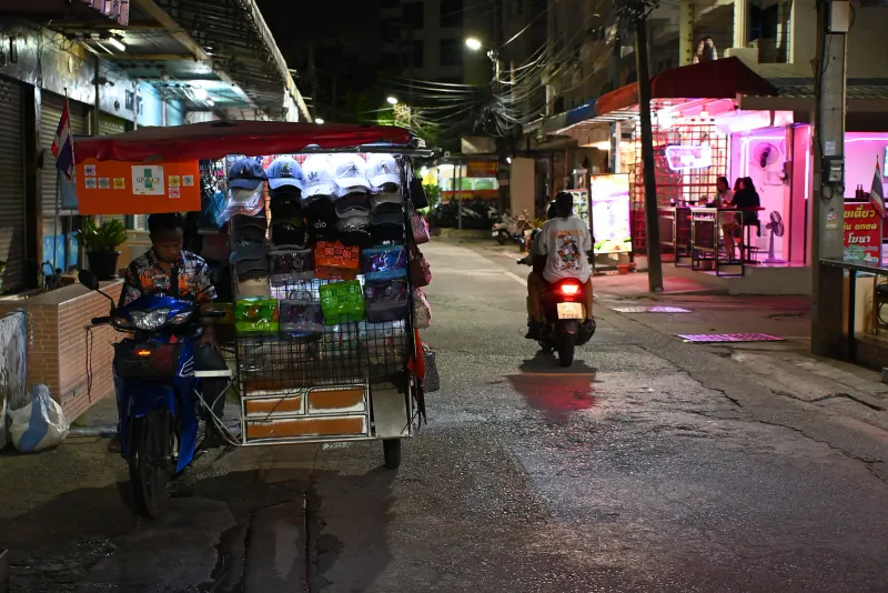 Motociclista con un bambino piccolo dietro, con un casco dai colori vivaci, in una strada thailandese trafficata