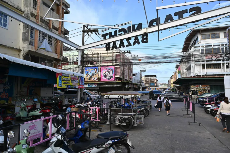 File di scooter parcheggiati dietro barriere rosa in una strada di mercato thailandese di giorno