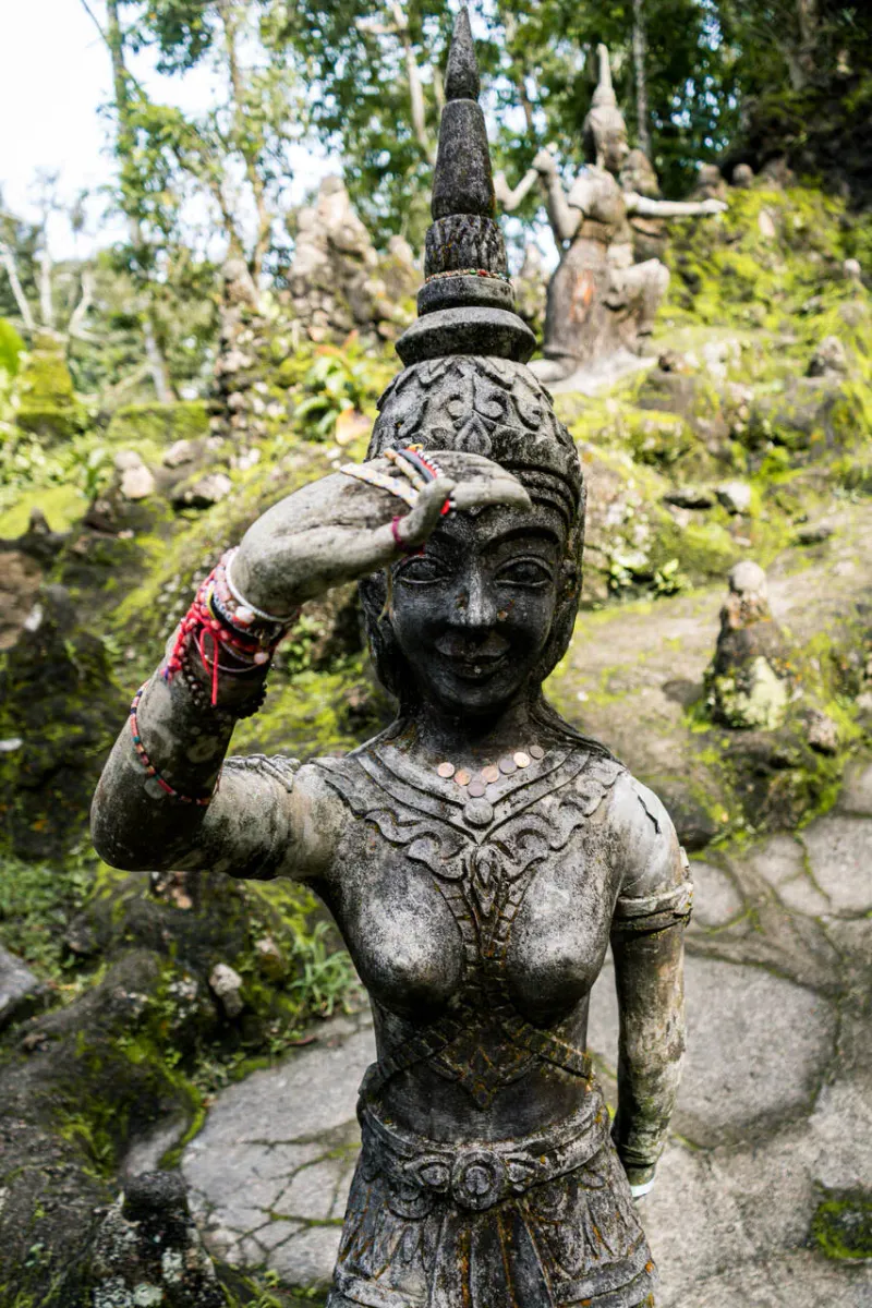 Verwitterte Steinfigur mit Opfergaben von Besuchern im Secret Buddha Garden