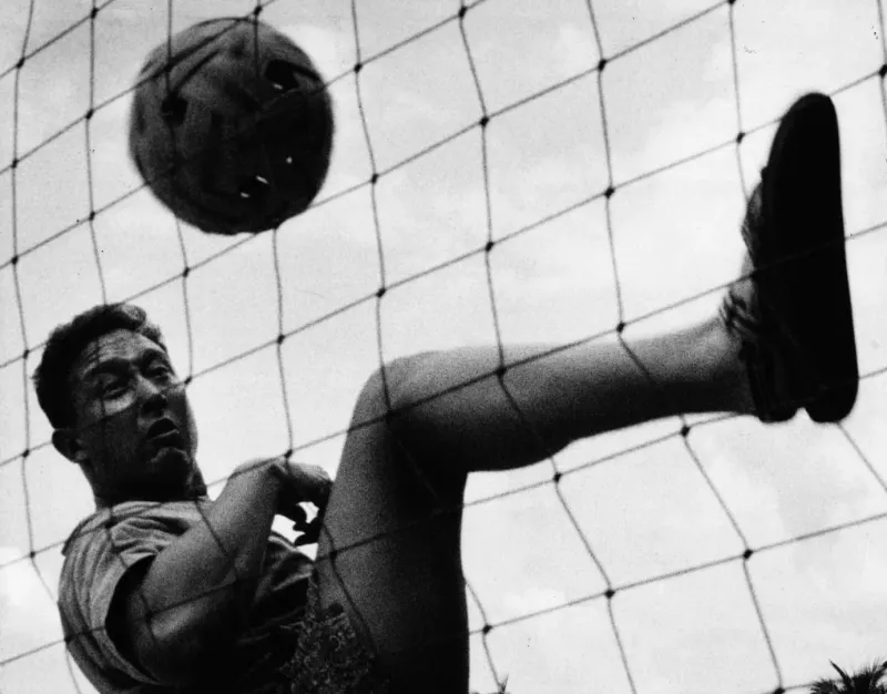 Archival black-and-white photo of a player performing an overhead kick during a takraw match in Thailand