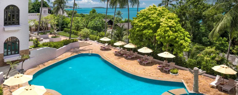 Piscina azzurra curva con lettini e ombrelloni sopra la baia allo Sheraton Samui Resort