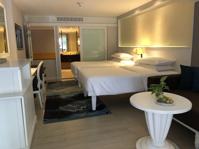 Letti singoli con lenzuola bianche, un pannello testiera a onde e un bagno aperto dietro una porta scorrevole satinata allo Sheraton Samui Resort