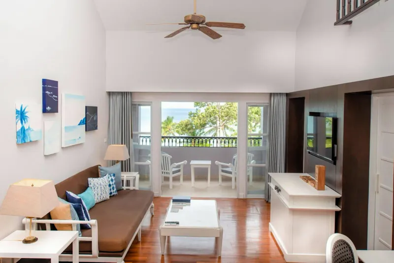 Salotto di una suite su due livelli con divano letto marrone, ventilatore a soffitto e un balcone sul mare allo Sheraton Samui Resort
