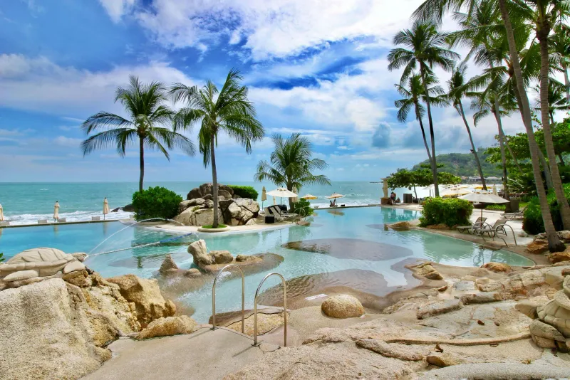 Piscina bassa con bordi di roccia, sculture di tartarughe in pietra e palme di fronte al mare allo Sheraton Samui Resort