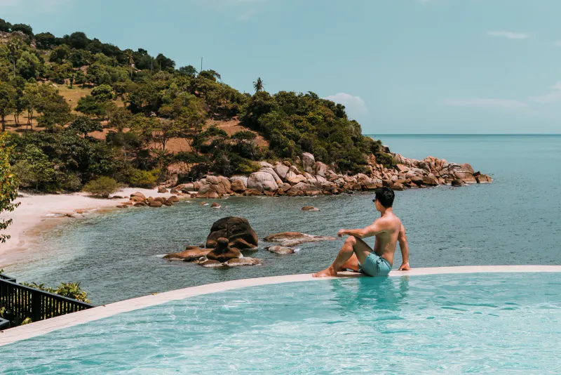 Bordo di una piscina a sfioro sopra un promontorio roccioso e una baia di sabbia sulla costa di Koh Samui