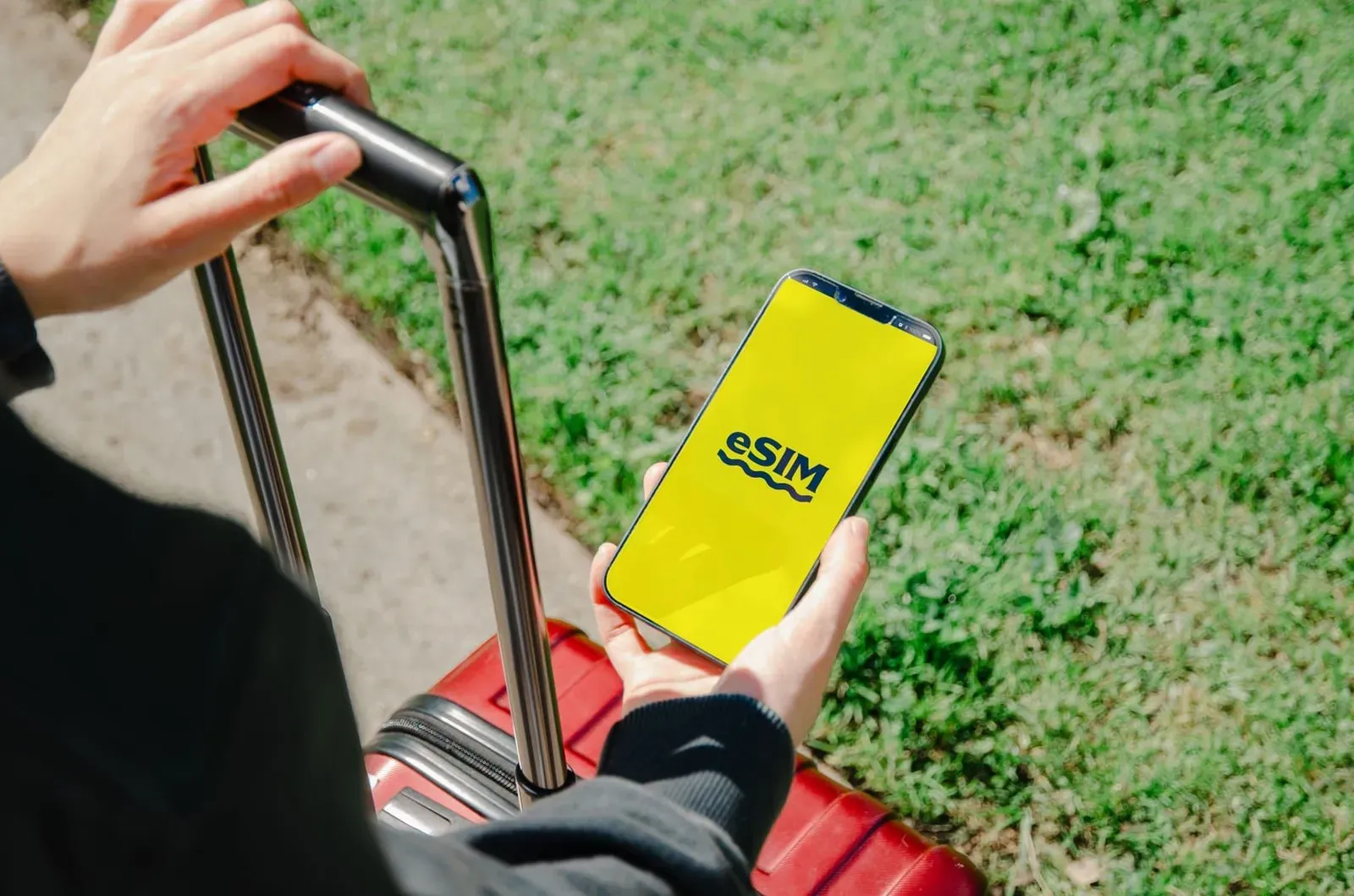 Traveler holding a smartphone showing an eSIM activation app while standing with luggage