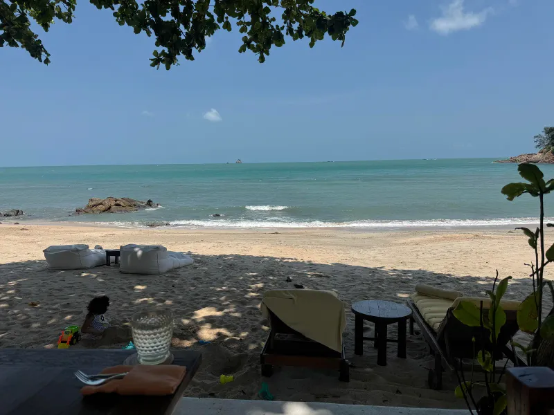 Spiaggia di sabbia a Samrong Bay, a Koh Samui, con sdraio e un mare turchese calmo