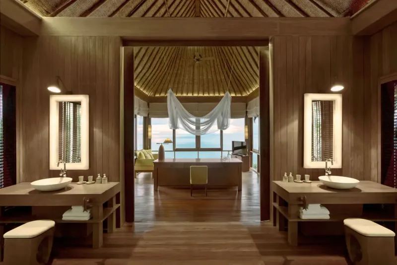 Bagno di legno di una villa del Six Senses Samui con due lavabi e una vasca con vista mare dietro le tende