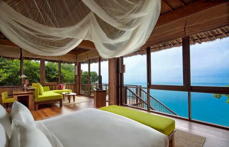 Camera da letto di una villa con piscina del Six Senses Samui, con zanzariera, lettino verde e vista mare a tutta parete