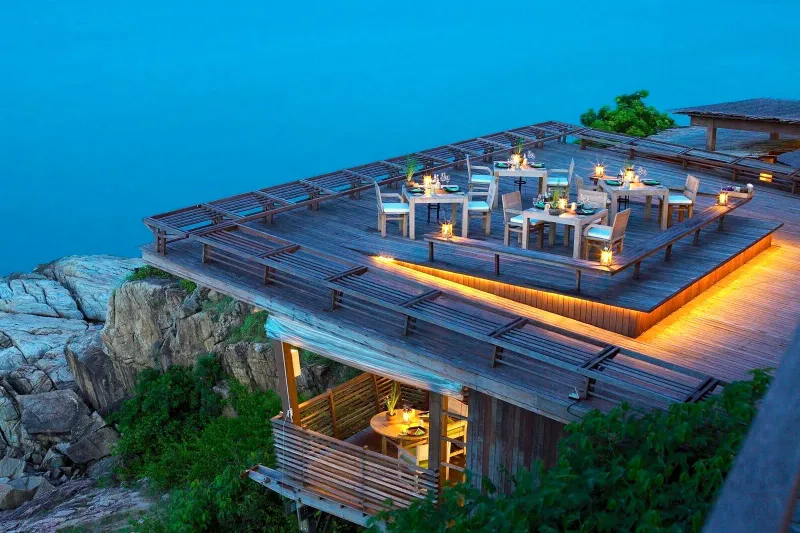 Terrazza ristorante a picco sul mare del Six Senses Samui, illuminata al crepuscolo sopra gli scogli e il mare