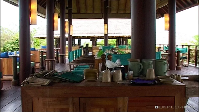 Ristorante all'aperto del Six Senses Samui con colonne di legno, un banco del buffet e tetti di paglia