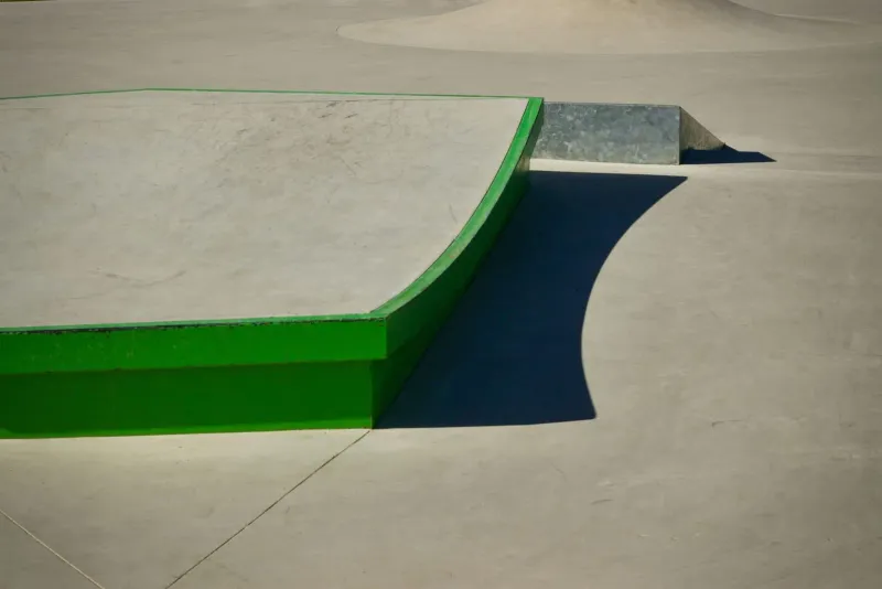 Modern skatepark with a curved green ramp under bright sunlight