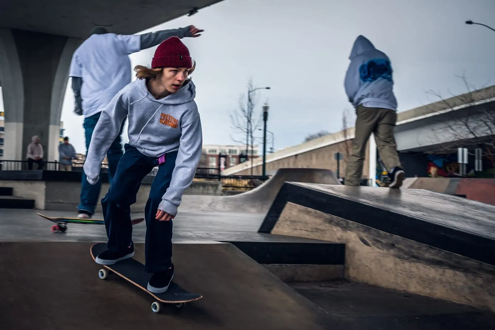 Teenager skateboarding at an urban skate spot in dappled shade under a bridge or overpass