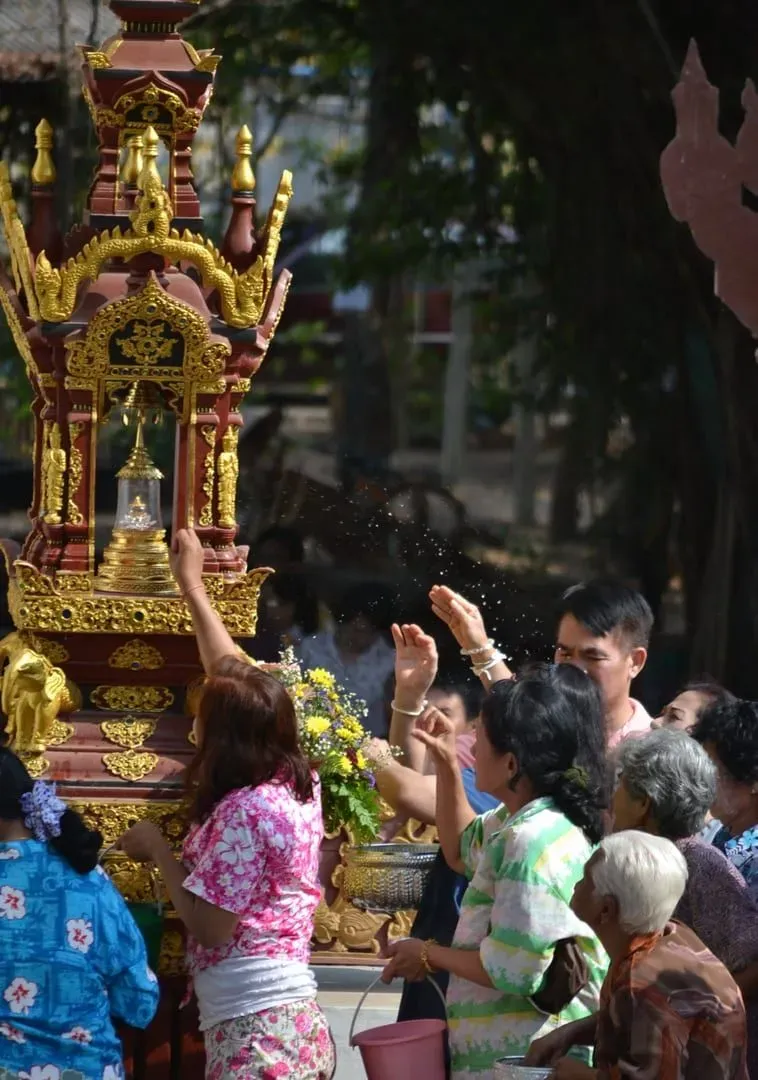 Thai locals gathered at a temple pouring water over a Buddha statue during Songkran celebrations