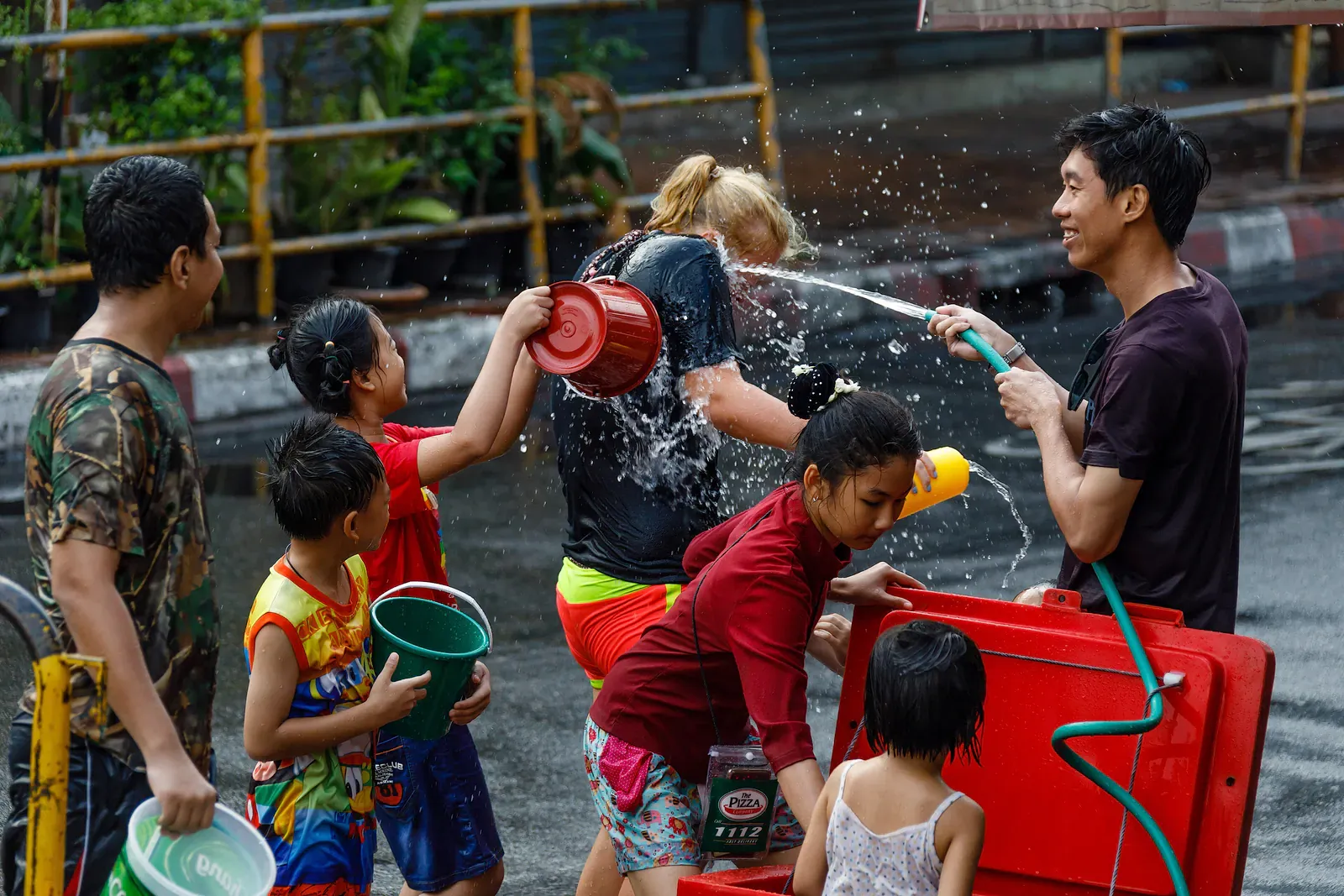 Children and adults splashing each other with buckets and hoses during a Songkran water fight in Thailand