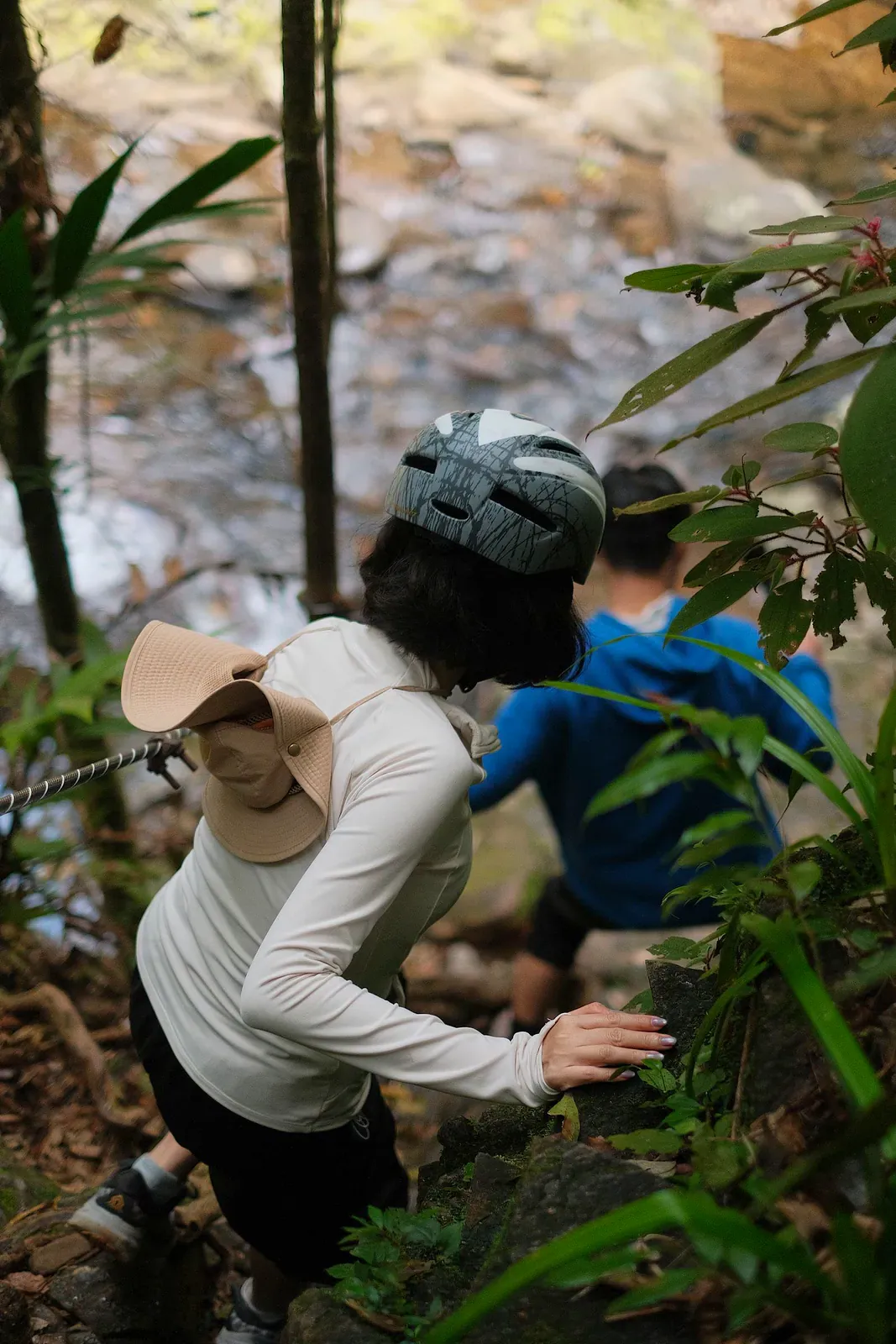 Excursionistas trepando por un sendero de selva empinado y rocoso cerca de un arroyo forestal