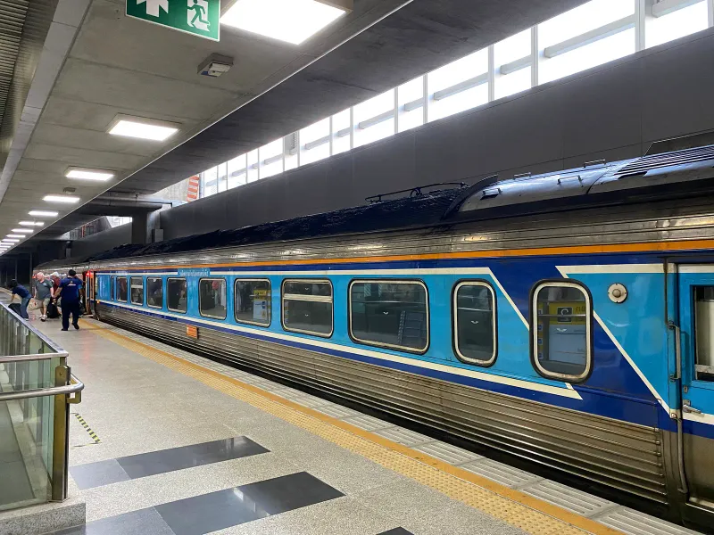 Voiture bleue d'un train interurbain thaïlandais à quai dans une gare, des passagers montent