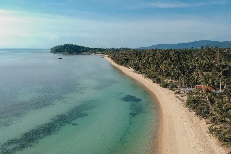 Luftaufnahme des von Palmen gesäumten Sandes und Riffs bei Taling Ngam