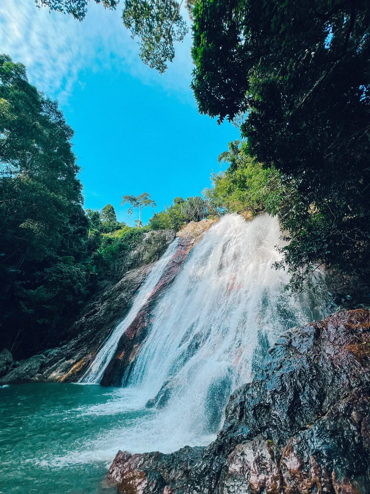Sonniger Dschungelwasserfall stürzt in ein klares Gumpenbecken