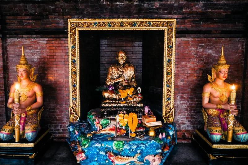 Gilded shrine with kneeling deva statues holding candles inside a brick alcove