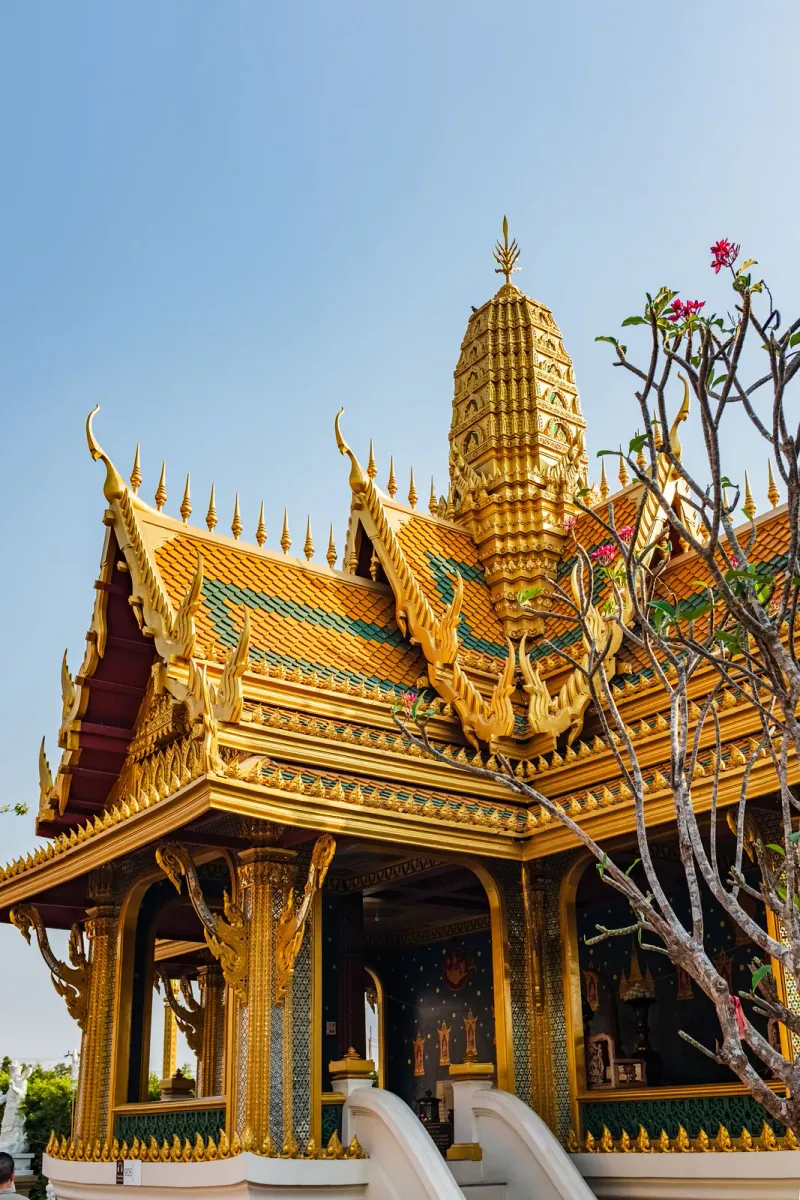 Golden multi-tiered chedi spire against a blue sky, flanked by a flowering tree