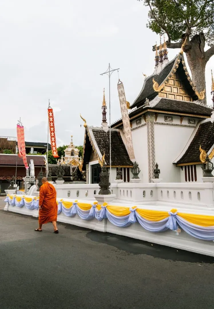 Monk walking past an ornately decorated temple in Chiang Mai's old city during this Thailand two week itinerary