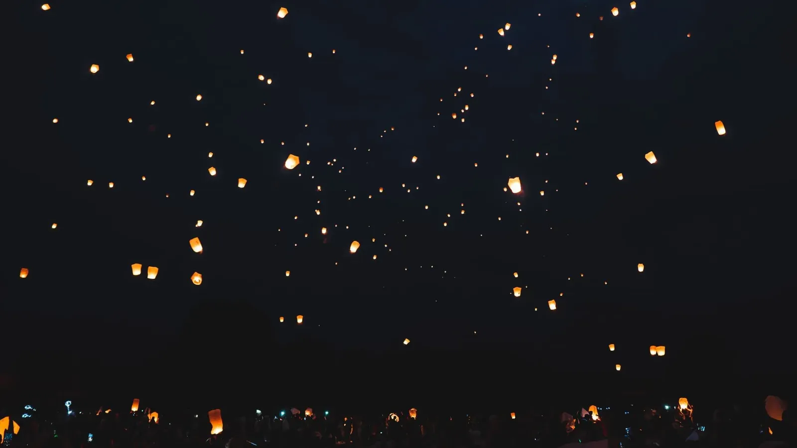 A mesmerizing view of illuminated sky lanterns floating against a dark night sky during a festival.