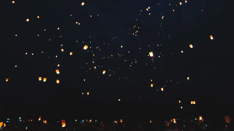 Illuminated sky lanterns floating against a dark night sky, evoking Koh Samui's Loy Krathong festival evening