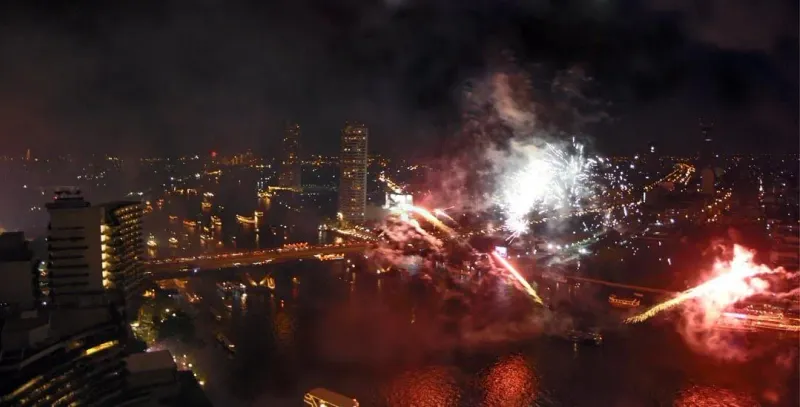 Loy Krathong evening celebration in Thailand with fireworks and floating candle rafts on the water