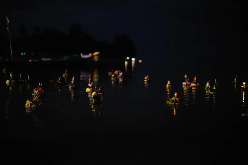 Illuminated krathongs floating on dark water during a Thailand Loy Krathong night festival