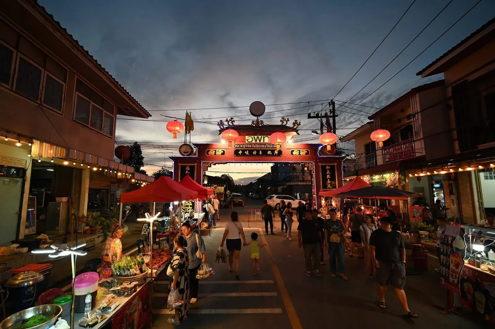 Lantern-lit night market archway with food stalls and evening shoppers, similar to a Koh Samui walking street