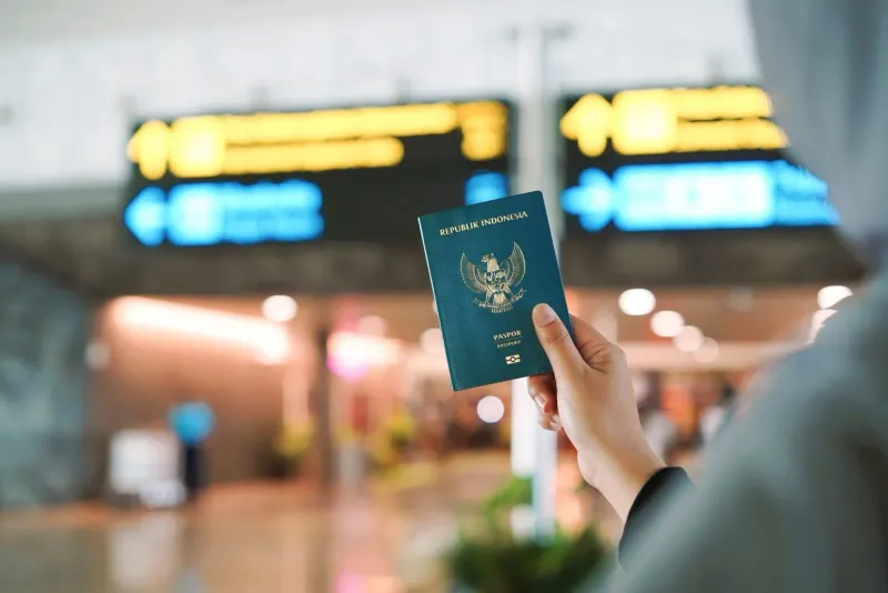 Traveler holding a passport at a busy Southeast Asian airport terminal before a Thailand visa check