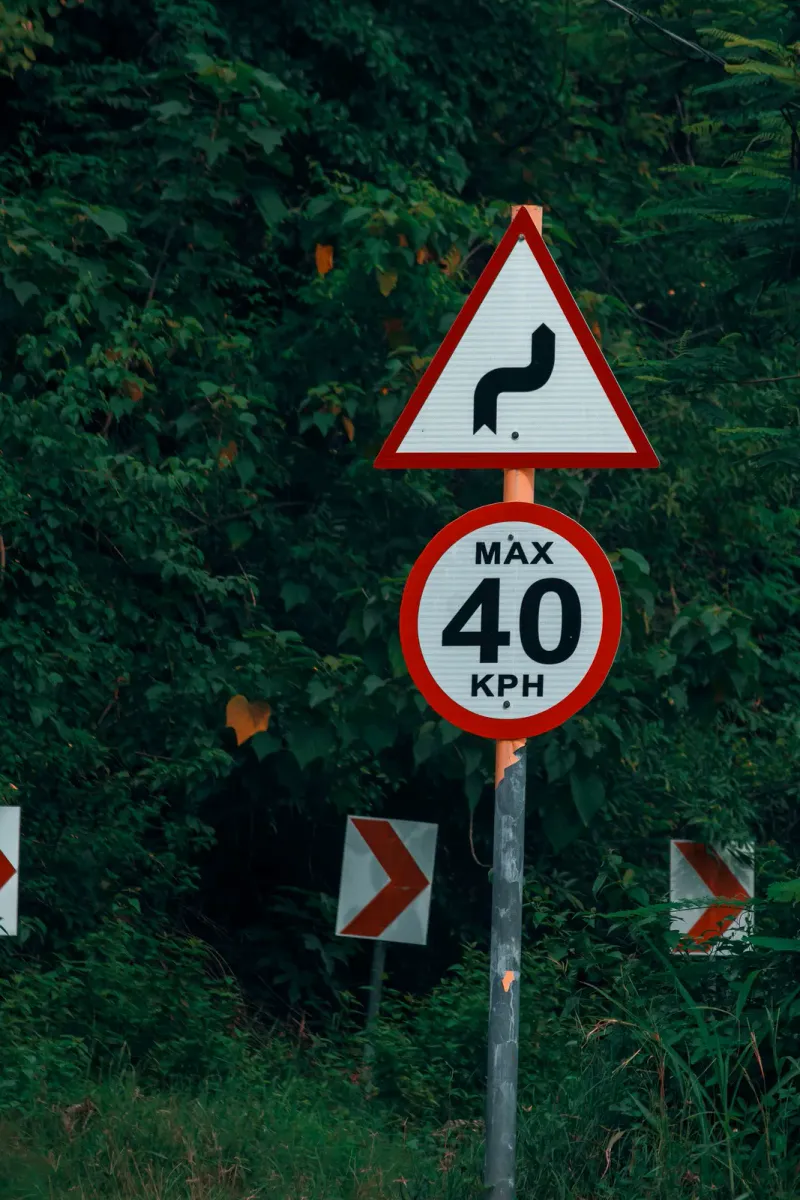 Panneau de virage dangereux au-dessus d'un panneau de limitation à 40 km/h, près de flèches chevrons sur une route de forêt