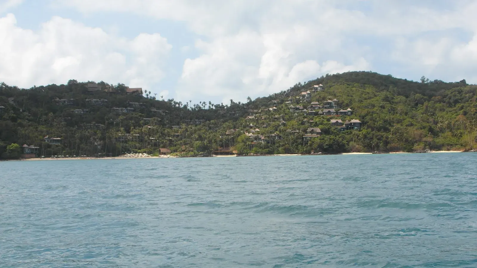 Resort villas terraced into a green hillside above a bay on Koh Samui's Laem Yai coast, seen from the water