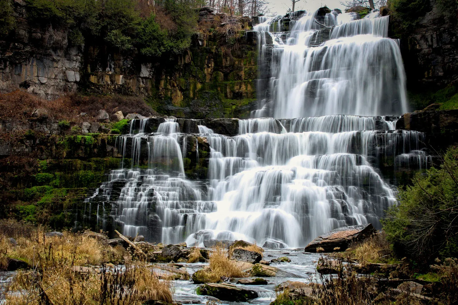Ein mehrstufiger Wasserfall stürzt über moosbewachsene Felsen im dichten Dschungel