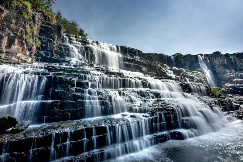 Waterfall flowing over tiered rocks under a bright sky