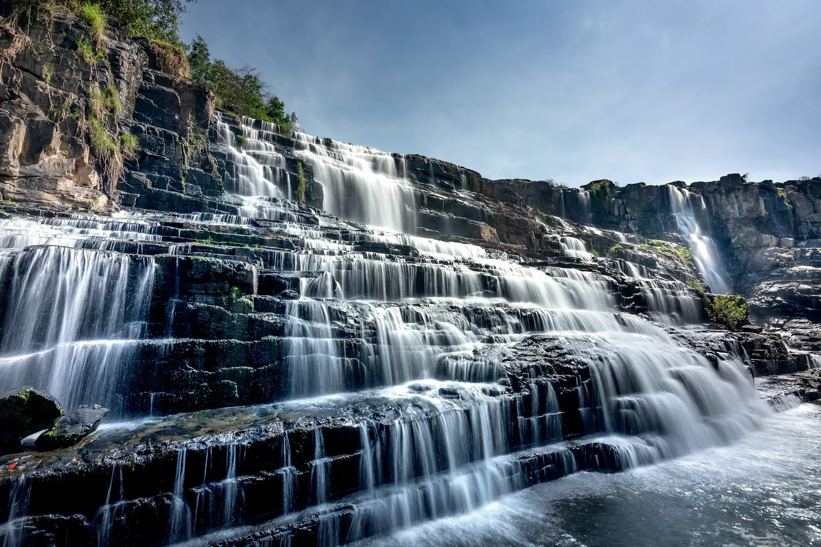 Wasserfall fließt über gestufte Felsen unter hellem Himmel