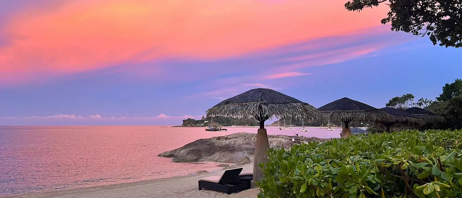 Rosa-violetter Sonnenuntergangshimmel über Tong Sai Bay mit Strandschirmen mit Reetdach als Silhouette