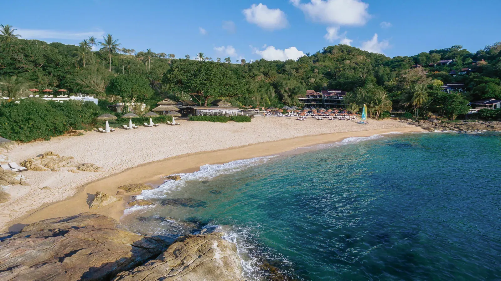 Blick auf Augenhöhe über den Sand und die Resortgebäude von Tong Sai Bay unter einem schattenspendenden Baum