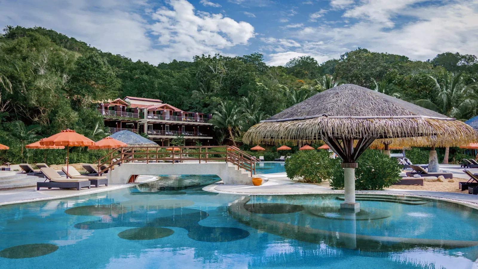 Resort-Swimmingpool mit strohgedeckter Sala und Liegestühlen unterhalb des Hangs