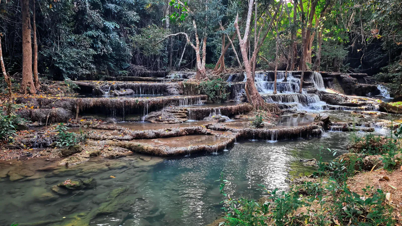 Tropischer Waldwasserfall über gestufte Felsterrassen in klare Pools