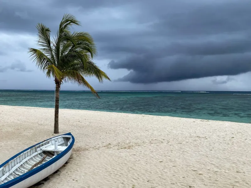 A small boat resting on a windy Koh Samui beach with palm trees under gathering storm clouds