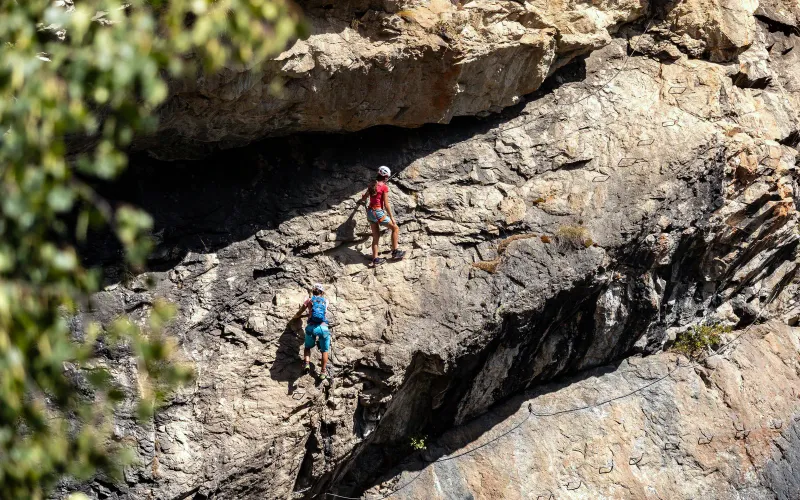 A hiker climbing a steep rock face using fixed ropes in a jungle setting