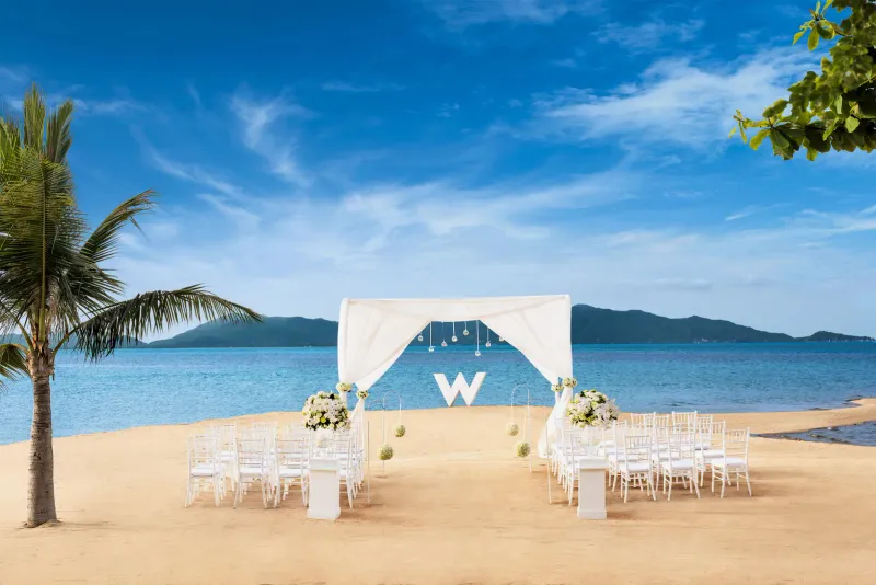 Installation de mariage sur la plage du W Koh Samui, avec chaises blanches, une arche et l'île derrière