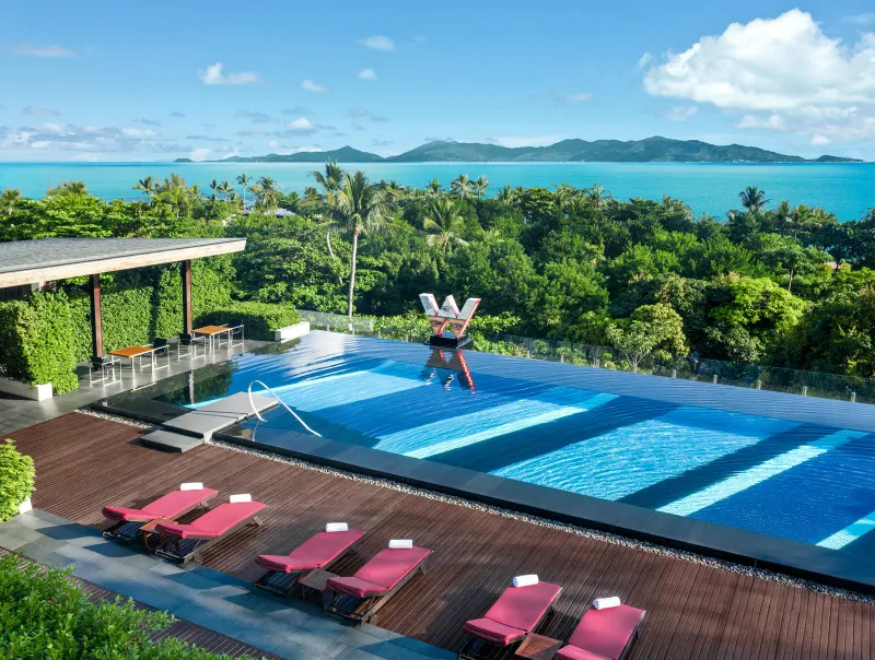 Vue aérienne d'une piscine infinity du W Koh Samui, avec transats rouges, le logo W, la mer et les îles derrière