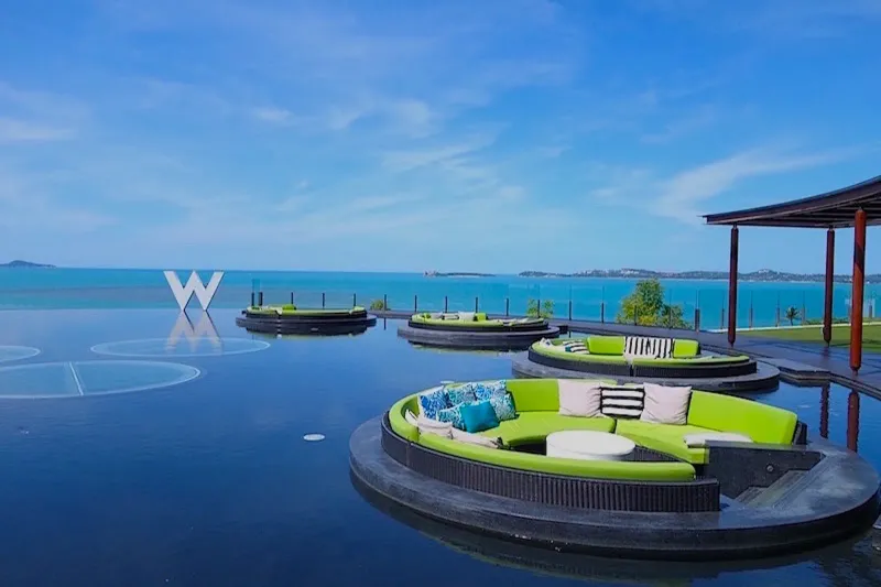 Canapés verts ronds flottant dans la piscine miroir du W Koh Samui, avec le logo W et la mer derrière
