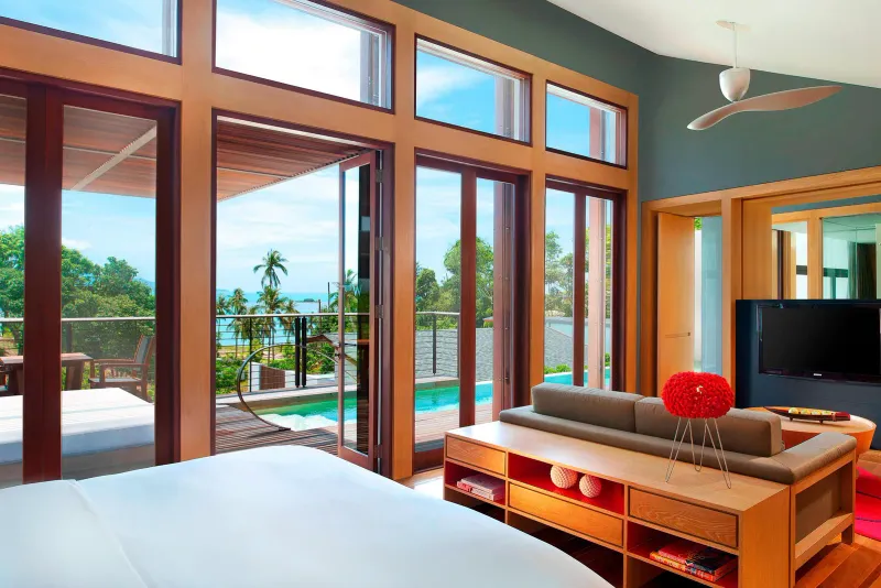 Chambre et salon d'une villa du W Koh Samui, avec baies vitrées du sol au plafond, touches de rouge et terrasse avec piscine